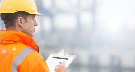Man dressed in a high visibility jacket and a hard hat using a clipboard