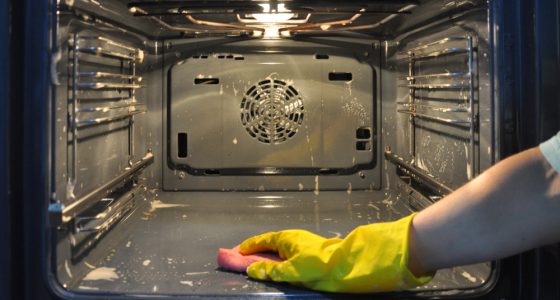 Man with yellow rubber gloves scrubbing the inside of an oven