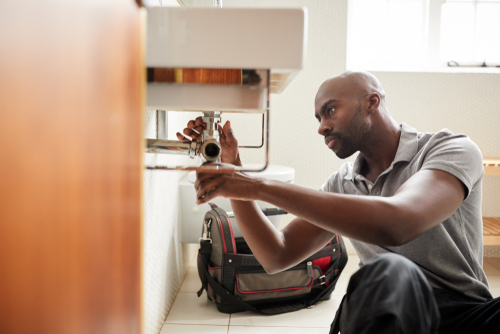 Male plumber in bathroom fixing pipes under a sink