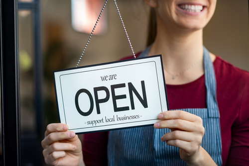 Female shop owner turning sign on entrance to say "We are open"