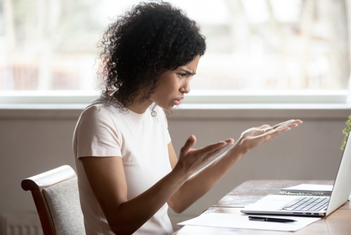 Woman looking frustrated on laptop, hands gesturing that she is not happy